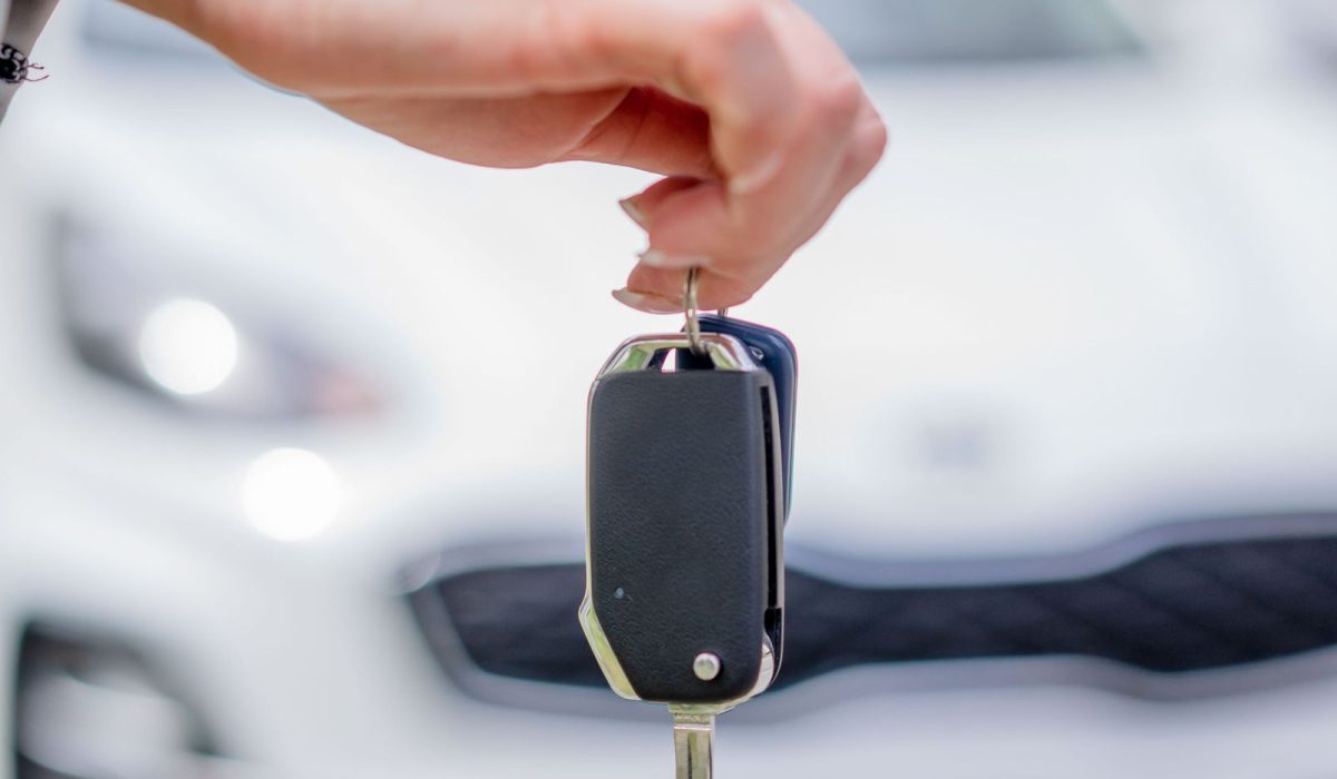 Person holding a car key with a rental vehicle behind them