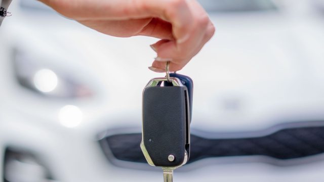 Person holding a car key with a rental vehicle behind them